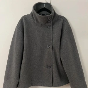 Kappa - Snygg grå jacka från Gina Tricot i ullblandning med hög krage och asymmetrisk knäppning framtill. Perfekt för kyliga dagar när du vill ha en stilren look.