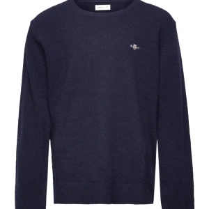 Mörkblå stickad tröja från GANT - Säljer en klassisk mörkblå stickad tröja från GANT med rund halsringning och diskret logga broderad på bröstet. Tröjan har lång ärm och är perfekt för lager-på-lager-stil. Enkel och stilren design som funkar till det mesta.