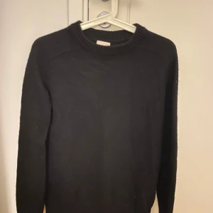 Svart stickad tröja - En klassisk svart stickad tröja med rund halsringning och ribbade muddar. Tröjan har en enkel och stilren design med lång ärm, perfekt att matcha med jeans eller kjol. Passformen är normal och materialet känns mjukt och bekvämt.