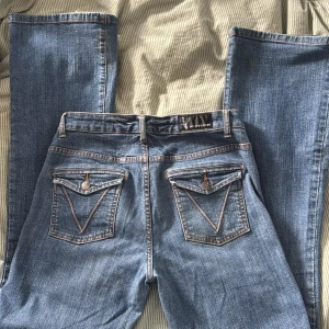 Blå straight leg jeans från 365 Sunshine - Snygga blå jeans från 365 Sunshine i modellen Cecilia Straight Leg. Klassisk femficksdesign med coola bakfickor med lock och knapp. Jeansen är i stretchig denim. Står straight leg men skulle säga att det är mer bootcut/flare