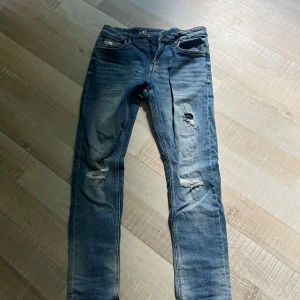 Blå slitna slim  jeans från LAB - Säljer ett par blå slim jeans från LAB med slitningar och hål på knäna. Jeansen har klassisk femficksdesign, normal midja och är tillverkade i stretchig bomull för en tajt passform. Perfekta för en avslappnad och trendig look. Är i stolek 164!