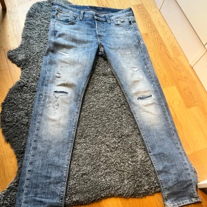  Jack & Jones 32/32 - Säljer ett par blå jeans från Jack & Jones i storlek 32/32. Jeansen har slitna detaljer, små hål och ljusa partier för en riktigt avslappnad vibe. Klassisk femficksmodell med raka ben och snygga sömmar på bakfickorna. Perfekta för dig som gillar en streetig look.