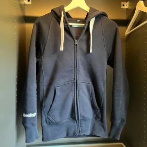 Mörkblå hoodie från Russedress XS - Mörkblå hoodie från Russedress i storlek XS. Tröjan har dragkedja, huva med vita snören och två stora fickor framtill. Långärmad modell i mjuk bomullsblandning, perfekt för chill dagar. Diskret logga på ärmen för en clean look. Osäker på om ja ska sälja men kom med bud! 