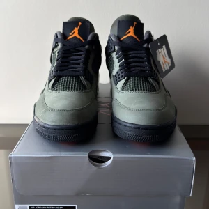 Air Jordan 4 x UNDEFEATED (2025) - 🔥 En av de mest hypade Jordan-releaserna 2025. Premium mocka, militärgröna detaljer och klassisk Jordan 4-heritage = direkt grail. ✅ Deadstock / Helt nya – aldrig provade 📦 Originalkartong + tillbehör medföljer: Orangea snören + UNDFTD Hangtag 💯 100% äkta  Perfekt för samlare eller för dig som vill flexa en av årets hetaste drops.