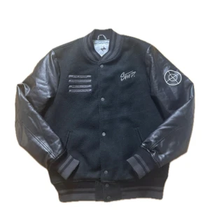 Jacka - Svart bomberjacka från Pull&Bear SWTD med feta skinnärmar och broderad logga på ryggen. Jackan har tryckknappar, ribbade muddar och coola detaljer framtill. Perfekt för dig som vill sticka ut med streetstyle-vibe.