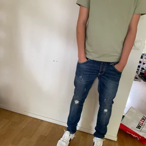 Blå skinny jeans med slitningar - Säljer ett par blå skinny jeans med snygga slitningar och lätt tvättad look. Jeansen har klassiska fem fickor, normal midja och smal passform hela vägen ner. Perfekta för dig som gillar en modern och avslappnad stil.