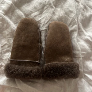 Bruna pälsfodrade tumvantar - Säljer ett par bruna tumvantar med mjuk päls runt mudden. Vantarna är tillverkade i mocka och har en klassisk form med grova sömmar. Perfekta för kalla vinterdagar när du vill hålla händerna riktigt varma. Vantarnas mått: Handbredd: 24 cm | Handlängd: 21 cm.