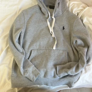 Grå Ralph Lauren hoodie M - Säljer denna gråa Ralph Lauren hoodie i storlek M. Den är perfekt nu till hösten på grund av att hur varm den är. Hoodien är stilren och tidslös vilket gör att man kan ha den oavsett tillfälle. När man är hemma och tar det lugnt men ändå vill vara snygg eller när man ska gå ut och vill se stilig men avslappnad ut. 