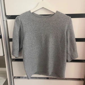 Grå stickad tröja från ONLY - Säljer en grå stickad tröja från ONLY i storlek S. Tröjan har rund hals, ribbade muddar och halvlånga ärmar med lätt puff vid axlarna. Perfekt för dig som gillar enkel och stilren look med lite extra detalj på ärmarna.