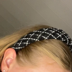 Svartvitt rutigt diadem - Snyggt diadem i svart och vitt med rutigt mönster. Diademet har en lite bredare form och är klätt i ett tyg som ger en trendig och cool känsla. Perfekt accessoar för att lyfta din look och hålla håret på plats.