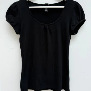 Svart topp med puffärm - En svart topp från H&M med rund halsringning och korta puffärmar. Toppens enkla design gör den lätt att matcha och den är sydd i mjuk bomull som känns skön mot huden. Perfekt för dig som gillar en stilren look med en liten twist.