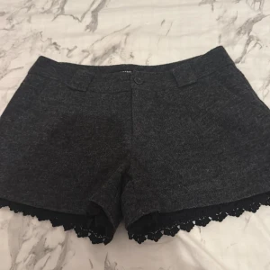 Mörkgrå shorts med spets från Koton - Snygga mörkgrå shorts från Koton med dekorativ svart spetskant nedtill. Klassisk passform med knapp och hällor för bälte. Perfekta för dig som vill ha en stilren men ändå unik look.