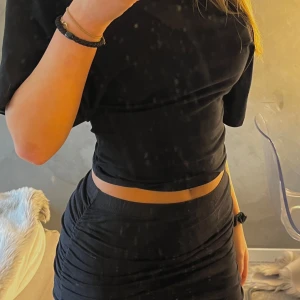 Svart tight kortkjol med rynkade sidor - Säljer en svart tight kortkjol med snygga rynkade detaljer längs sidorna och även ibak. Kjolen har en enkel och stilren look som sitter figurnära och är perfekt att matcha med crop tops eller oversized tröjor.