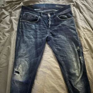 Dondup jeans - Säljer ett par mörkblå jeans från dondup med slitningar på benen för en cool, avslappnad look. Jeansen har klassisk femficksdesign, knappgylf och snygga detaljer på bakfickorna. 👍