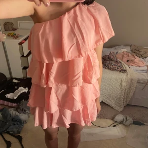 Rosa volangklänning oneshoulder - Supersöt rosa kortklänning med flera lager volanger och oneshoulder-design. Helt ny endast testad, aldrig använd. Då den va för kort för mig som är 170cm, storlek XXS/XS men passar storlek S också men på någon som är kortare💕 nypris 569kr