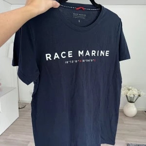 Mörkblå Race Marine t-shirt - Snygg mörkblå t-shirt från Race Marine med vit logga på bröstet. Klassisk rund hals och korta ärmar. Tillverkad i en mjuk blandning av bomull och polyester med lite stretch för extra komfort. Önskar du veta exakta mått? Tveka inte att höra av dig!