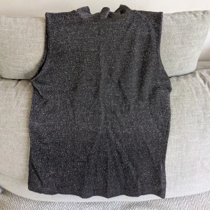 Glittrig svart polotopp från Peppercorn - Svart ärmlös polotopp med glittrigt mönster. Toppen har en tight passform och hög krage. Jag är ca 170 cm för referens. Vid köp av flera klädesplagg av mig samfraktar jag såklart!