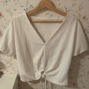Vit omlottopp med knyt framtill - En jättefin vit topp från zara med en knut nertill. Man kan välja hur hårt man vill ha den knuten. Den är lite rynkig i tyget med fina mönster. Jag har valfria använt den så därför säljas jag den. Pris kan diskuteras 