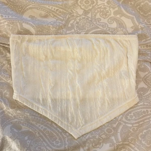 Champagnefärgad  tubtopp - Snygg  tubtopp i champagnefärgat tyg med lätt glans. Toppen har en spetsig nederkant och är elastisk upptill för att sitta på plats. Perfekt att styla med höga jeans eller kjol för en trendig look.