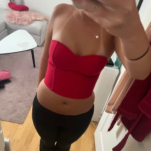 Röd korsettopp från NLY Trend - Snygg röd korsettopp från NLY Trend med markerade kupor och croppad passform. Toppen är axelbandslös och har dragkedja bak för enkel påklädning. Perfekt för dig som vill sticka ut med en färgstark look.