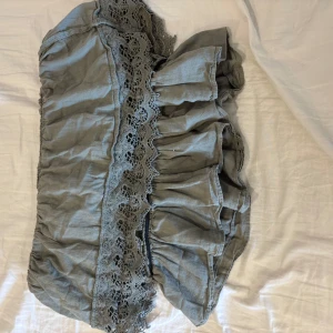 Grön volangtopp med spetsdetaljer - Supersöt grön offsholder topp med volanger och breda spetsdetaljer. Topp har en romantisk vibe och är perfekt för dig som gillar en feminin och bohemisk stil. Tillverkad i ett mjukt tyg som känns skönt mot huden.