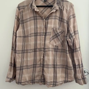 Beige rutig skjorta från H&M Divided - Snygg beige rutig skjorta från H&M Divided i storlek L. Skjortan har klassisk krage, bröstficka och knäppning framtill. Tillverkad i 100% bomull för en skön och luftig känsla.