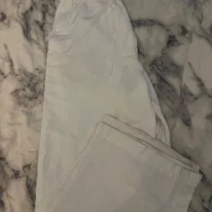 Vita vida linnebyxor med snörning - Säljer ett par  vita linnebyxor med bred passform och dragsko i midjan. Byxorna har elastisk midja och är perfekta för en chill och avslappnad stil. Luftiga och sköna, passar perfekt till sommaren. Tyvärr är de lite slitna och missfärgade vid fötterna, där av lägre pris. Jag är 155cm och de passar perfekt i längden, bortklippt lapp