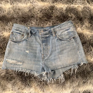 Levi's ljusblå jeansshorts med fransar - Ljusblå jeansshorts från Levi's med slitna detaljer och fransig rå kant nertill. Klassisk femficksmodell med knappar. Perfekta för sommaren och ger en avslappnad vibe.