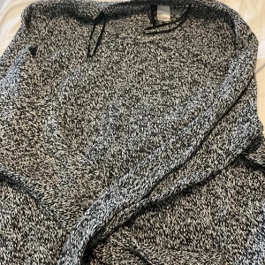 Svartvit stickad tröja Divided S - Mysig stickad tröja från Divided i svartvitt melerat garn. Tröjan har rund halsringning och långa ärmar, perfekt för lager på lager under kyliga dagar. Passformen är normal och materialet känns mjukt mot huden.