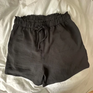 Svarta shorts med snörning - Svarta shorts med elastisk midja och snörning framtill. De har en avslappnad passform och är tillverkade i ett mjukt, lätt tyg som känns skönt mot huden. Perfekta för varma dagar eller när du bara vill chilla hemma
