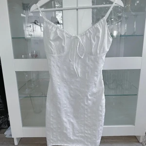 Vit finklänning - En vit finklänning med blom broderings liknande mönster som endast är testad och tvättad! Den har extra innertyg. Storlek XS men passar S! Där knytningen är, det är där man kan justera axelbanden. Nypris 129kr! FÖRST TILL KVARN!