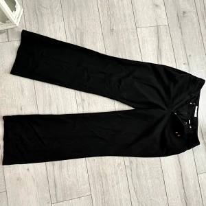 Svarta kostymbyxor från Esprit - Svarta kostymbyxor från Esprit med raka, vida ben och klassisk passform. Byxorna har diskreta bakfickor och stängs med knapp och dragkedja. Perfekta för en clean och stilren look. Materialet känns mjukt och följsamt.