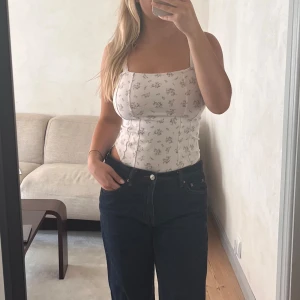 Blommig korsett-topp med lila detaljer - Supersöt korsettliknande-topp. Toppen har breda axelband, markerade sömmar och en figurnära passform. 🌸🌸🌸