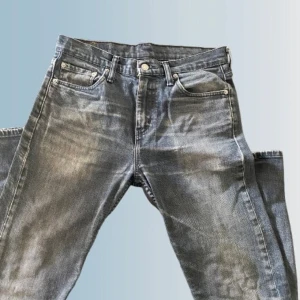 Levis 501 grå jeans med slitningar - Klassiska Levis 501 jeans i grått med snygga slitningar och vintagekänsla. Rak passform, fem fickor och knappgylf. Ikonisk Levis-lapp bak i midjan och röd etikett på bakfickan. Perfekta för en avslappnad och cool stil.