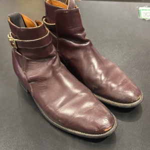 Vinröda Jodhpur boots från Mister Sargent - Snygga vinröda Jodhpur boots från Mister Sargent, tillverkade i England. Skorna har spänne runt ankeln, spetsig tå och låg klack. Tillverkade i skinn med klassisk design och kontrastsömmar. Perfekta för dig som gillar stilrena boots med en twist. Strl 9 UK men hyfsat små! 