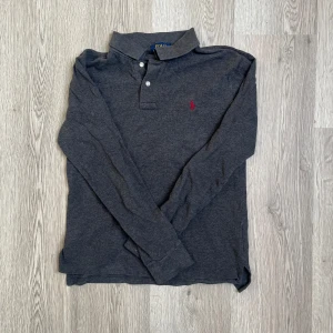Mörkgrå pikétröja från Polo Ralph Lauren - Snygg mörkgrå långärmad pikétröja från Polo Ralph Lauren. Är i storlek 14-16 i barn vilket motsvarar en Xs-S🤝🙌