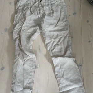 Beiga linnebyxor från Bondelid - Snygga beiga linnebyxor från Bondelid med avslappnad passform och dragsko i midjan. Perfekta för varma dagar med sin lätta känsla och klassiska look. Byxorna har fickor på sidorna och stängs med knapp och dragkedja.