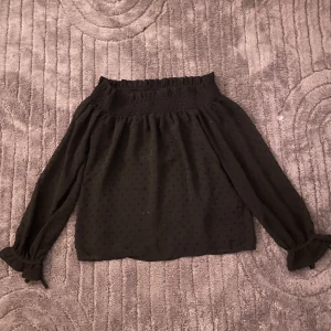 Svart offshoulder blus med prickar - Säljer en svart offshoulder blus med diskret prickigt mönster. Blusen har långa ärmar med volang och knyt vid ärmsluten💕