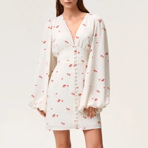 Vit blommig kortklänning med v-ringning - Säljer denna klänning från adoore då jag vill köpa i en annan storlek. En superfin vit kortklänning med små röda blommor, v-ringning och långa puffärmar. Klänningen har knappar framtill och markerad midja som ger en snygg siluett. Perfekt för sommarens alla tillfällen! Använd 1 gång