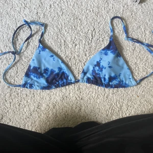 Blå tie-dye trekantsbikini XS - Snygg trekantsbikini i blå tie-dye mönster med smala knytband i nacken och ryggen. Bikinin är i mjukt och stretchigt material som sitter skönt och är perfekt för stranden eller poolen. Färgerna går i ljusblått och mörkblått för en fräsch sommarkänsla.