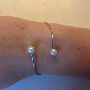 Silvrigt armband och ring med pärlor - Säljer ett minimalistiskt silvrigt armband med två vita pärlor i ändarna och en matchande enkel silvrig ring. Båda har en stilren, lite oregelbunden form som ger en cool och modern känsla. Perfekt för dig som gillar enkel men snygg design. Armbandet är justerbart! De är handgjorda!💕