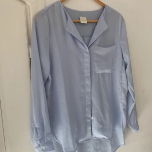 Ljusblå skjorta - Stilren ljusblå skjorta med klassisk krage, bröstficka och knappar framtill. Materialet är tunt och lätt genomskinligt.