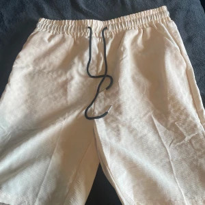 Beiga shorts med snörning - Snygga beiga shorts med elastisk midja och svart snörning framtill. De har en rak passform och är tillverkade i ett lätt tyg som passar perfekt för varma dagar. Shortsen har fickor på sidorna och en stilren, enkel look.