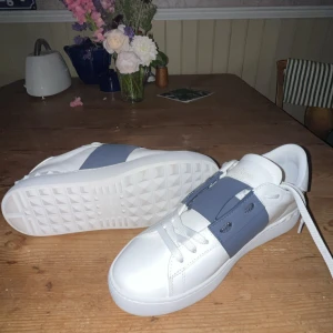 Valentino Garavani  - Snygga vita sneakers från Valentino Garavani med marin blå detalj över snörningen. Säljer de jag fick de i present och de inte passade. Aldrig använda bara testade 