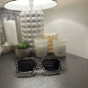 Gråa kantiga solglasögon - Snygga solglasögon med transparent grå båge och svarta glas. De har en modern, kantig form som ger en cool vibe. Perfekta för att lyfta din stil under soliga dagar.