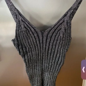 Glittrig svart ribbad linne - Supersnygg svart glittrig linne från design by si med ribbad struktur och smala axelband. .