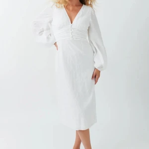 GinaTricot Långklänning - Superfin vit långklänning från Gina Tricot med v-ringning, markerad midja och knappar framtill. Väldigt lik Adoore-klänningarna i modellen. Endast använd en gång, helt slutsåld från förra året.