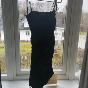 Svart klänning från Adoore - Supersnygg svart klänning från Adoore med smala axelband som knyts på axlarna. Rynkade detaljer längs sidorna och en dragkedja för att få en figurnära passform. Sitter så himla fint och väldigt smickrande på kroppen. Helt ny och nypris 1800kr💖🌸 pris kan diskuteras