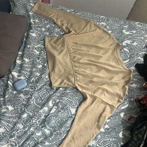 Beige långärmad croppad topp - Snygg beige croppad topp med långa ärmar och rund halsringning. Toppen sitter tajt i midjan och lösare upp till