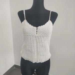 Vit virkad linnetopp - Supersöt vit virkad linnetopp med smala axelband och vågig spetskant både upptill och nertill. Toppen har en liten v-ringning framtill med två dekorativa hål och är perfekt för varma dagar. Ger en bohemisk och somrig vibe.